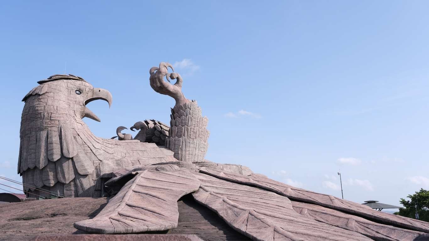 “Large stone eagle sculpture with wings spread and raised claw against a clear blue sky.”